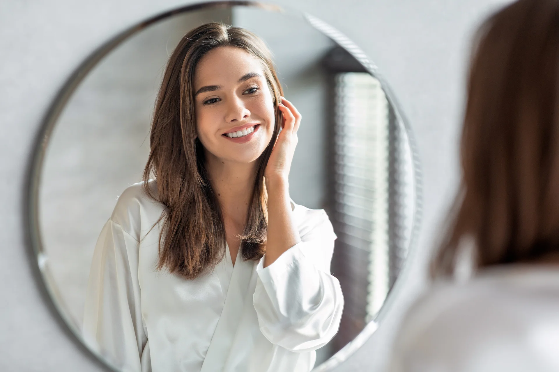 portait of a young woman smiling infront of the mirror||a woman who had cheek fillers at Dr. Lanna's clinic