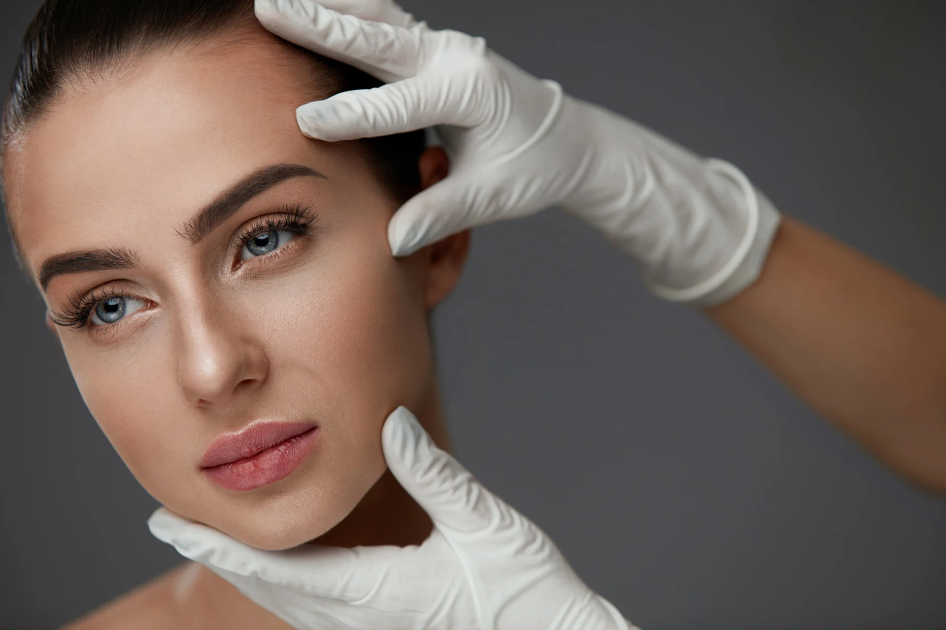 a portrait of a young woman and a pair of hands wearing white gloves holding her face||