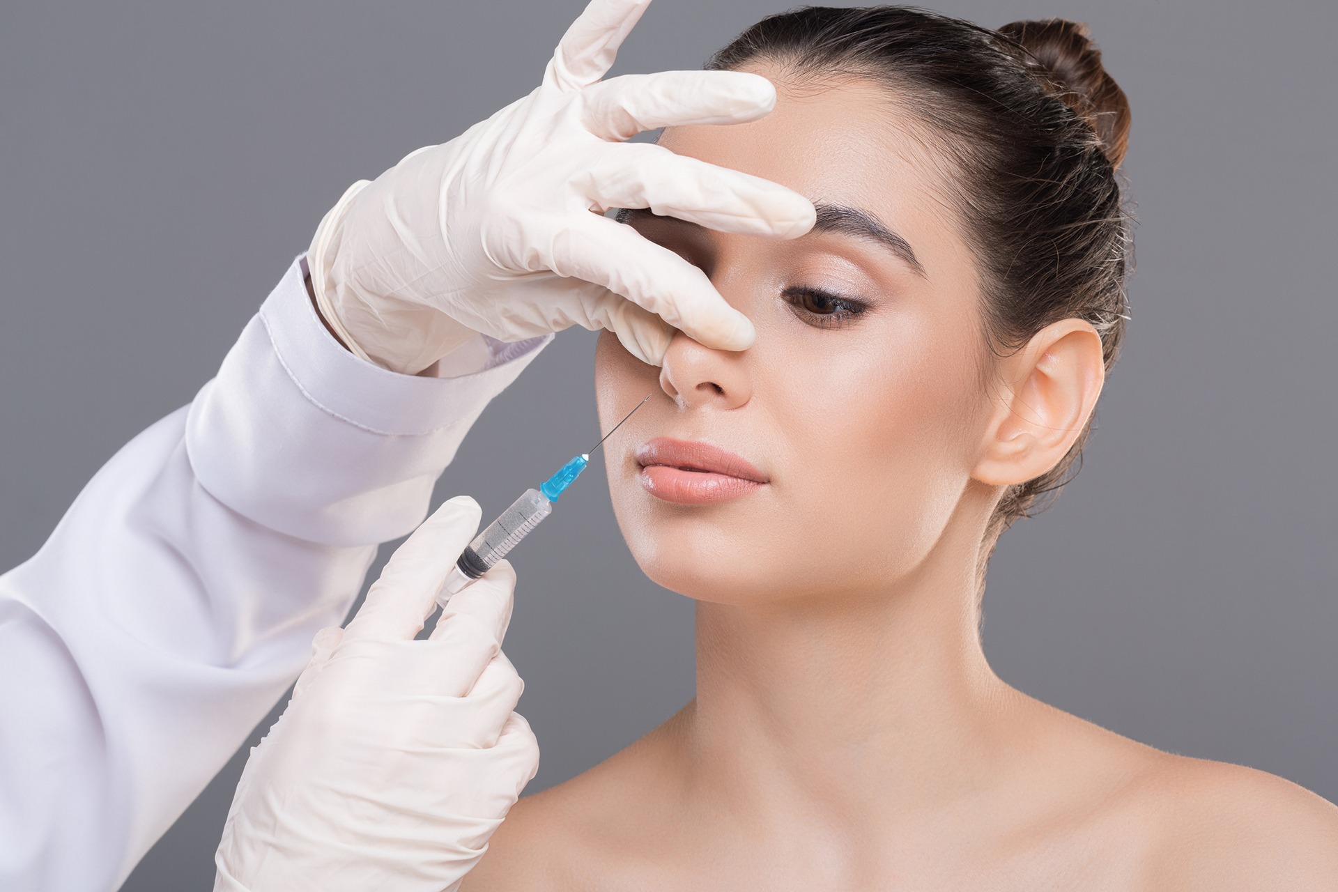 Woman getting filler injection to her nose|Woman getting dermal filler injection to the corner of her mouth|Young woman ready for rhinoplasty, doctor in blue gloves touching her nose|Filler treatment at Dr. Lanna Aesthetics