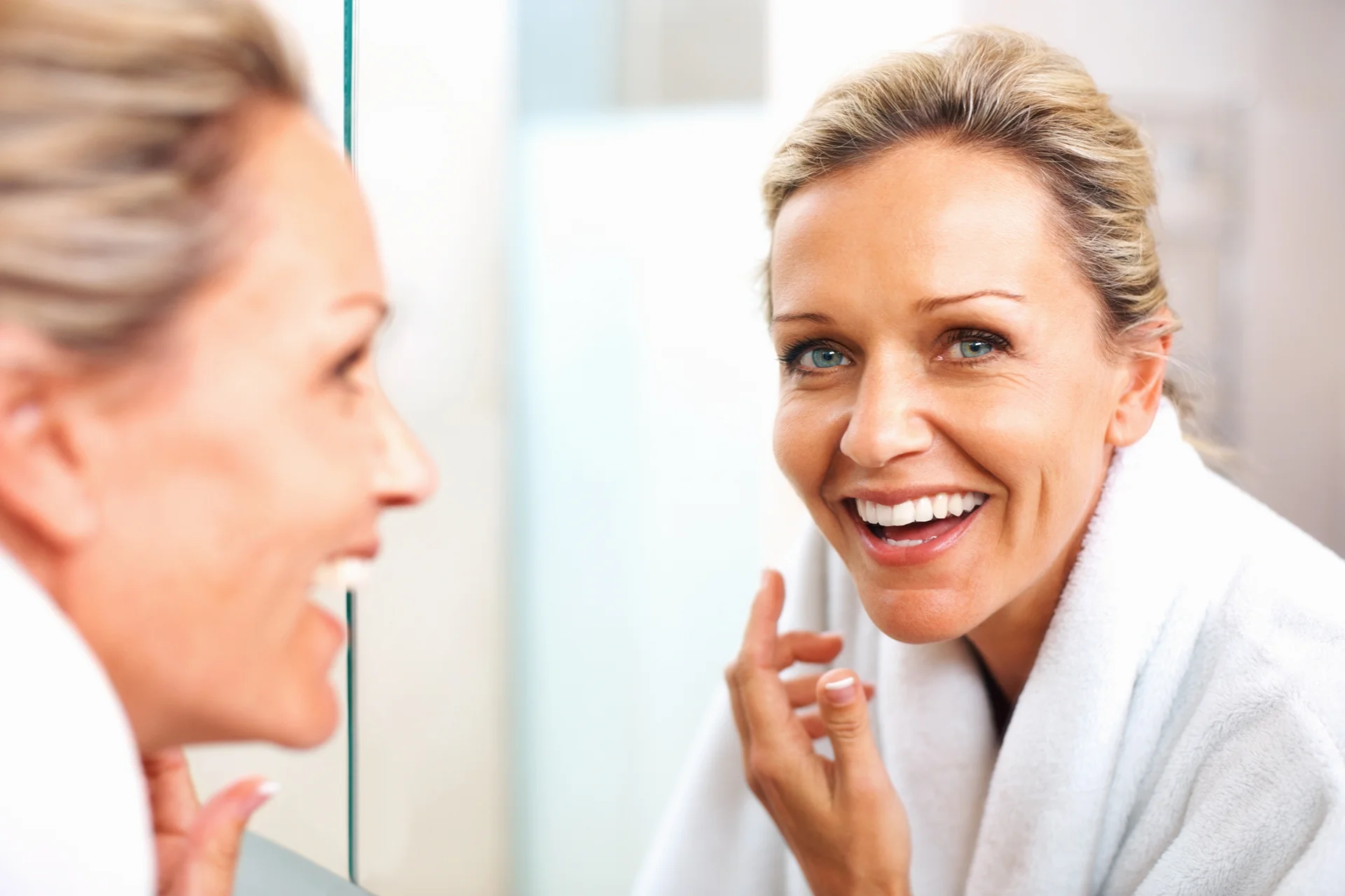 a matured woman smiling herself infront of the morror while checking out her face|a woman cleanses her face with cleanser|a woman received dermal filler treatment at Dr. Lanna's clinic