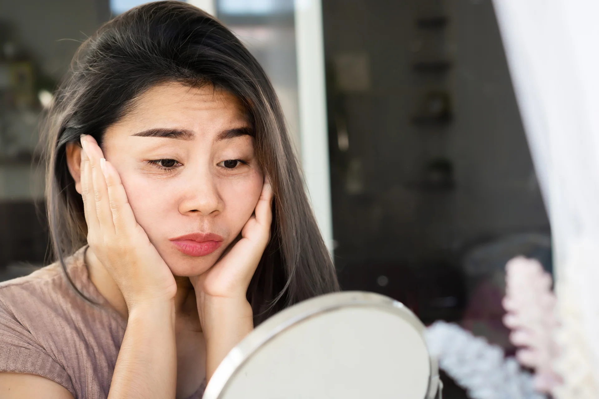 a woman looks at her swelling face in the mirror|doctor marks the patient's injection area of the face as they start the dermal filler treatment