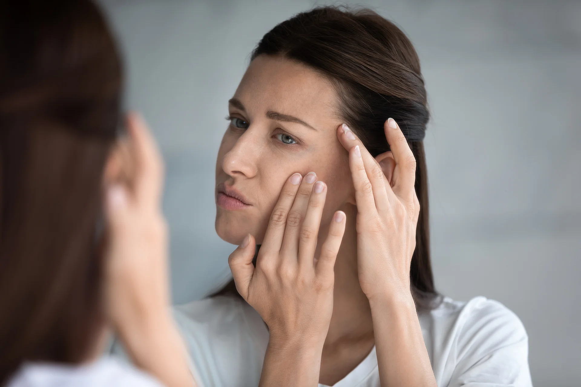 a woman checks her cheeks infront of the mirror|medicine and a glass of water|a woman had cheek filler treatment at Dr. Lanna's clinic