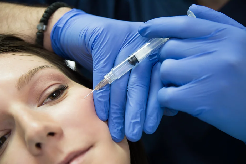 Gloved practitioner injecting cheek filler into a woman's face close-up