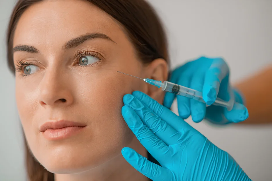 Gloved practitioner injecting filler into a woman's cheek
