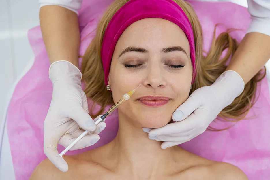 Gloved practitioner injecting filler near a woman's mouth