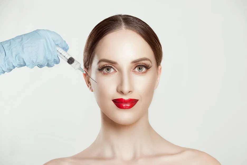 Gloved hand holding a syringe to a woman's face for filler