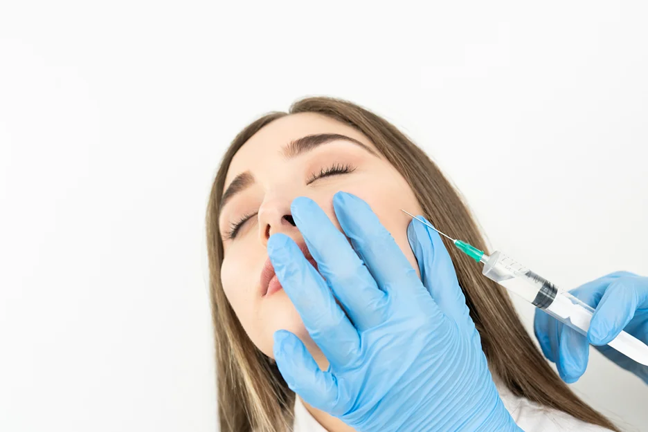 Gloved practitioner injecting filler into a reclining woman's cheek