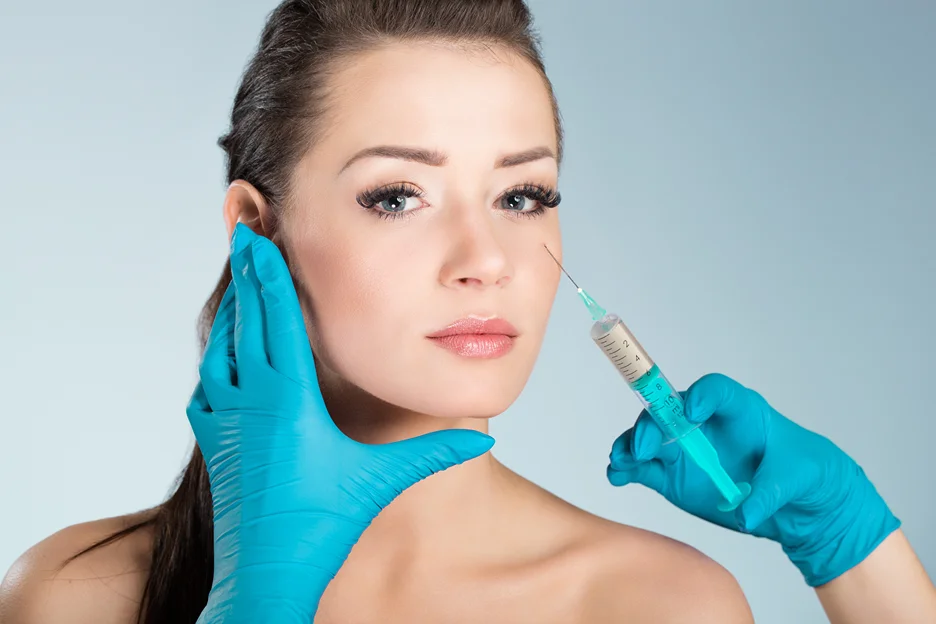 Gloved practitioner holding a syringe to a woman's face for filler